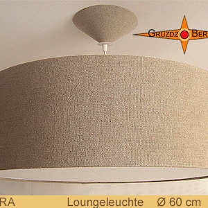 Könnte beinhalten: Eine Pendelleuchte mit einem beigefarbenen Stoffschirm in Trompetenform und einer weißen Innenverkleidung. Der Schirm hat einen Durchmesser von 60 cm. Die Leuchte ist mit "Cora" und "Loungeleuchte" beschriftet.