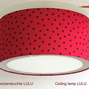 May include: A red ceiling lampshade with black polka dots. The lampshade is round and has a white interior. The text "Deckenleuchte LULU" and "Ceiling lamp LULU" is visible below the lampshade.
