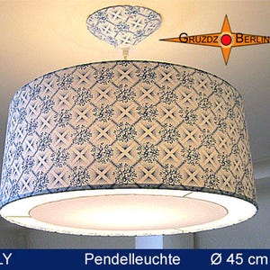 Può includere: Una lampada a sospensione cilindrica con un motivo a reticolo blu e bianco e dettagli floreali. La lampada include un rosone a soffitto abbinato e un diffusore bianco nella parte inferiore. Il testo "GRUZDZ BERLIN" e "HILLY" è visibile.