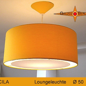 May include: A yellow cylindrical pendant light fixture with a white inner shade. The light is hanging from a white ceiling and has a diameter of 50 inches. The text "LUCILA Loungeleuchte Ø 50" is visible at the bottom of the image.