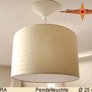 May include: A white fabric pendant light with a white ceiling mount. The light is 25 inches in diameter and has a striped pattern. The light is labeled "DORA Pendelleuchte Ø 25 cm" and "GRUZDZ BERLIN".