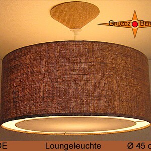 May include: A brown, cylindrical, fabric lampshade with a white inner lining. The lampshade is 45 inches in diameter. The lampshade is hanging from a white ceiling fixture. The text "GRUZDZ BERLIN" is visible in the background.