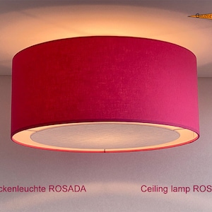 May include: A pink fabric ceiling lamp with a white inner shade. The lamp is labelled "Ceiling lamp ROSADA".