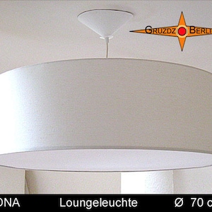 Könnte beinhalten: Eine große, weiße, zylindrische Pendelleuchte mit weißem Deckenbaldachin und Kabel. Der Text "GRUZDZ BERLIN" erscheint in einem orangefarbenen Stern-Logo, und der Text "LEONA Loungeleuchte Ø 70 cm" ist unten im Bild aufgedruckt.