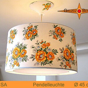 May include: A white pendant light with a floral print shade. The shade has a diameter of 45 cm and features a pattern of yellow and orange flowers on a white background. The light is suspended from a white ceiling fixture.