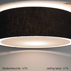 May include: A black drum-shaped ceiling lamp with a white interior and a bright light. The lamp is mounted on a white ceiling. The text "ceiling lamp UTA" is visible at the bottom of the image.