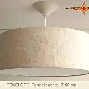 Könnte beinhalten: Eine beige zylindrische Pendelleuchte mit strukturiertem Stoffschirm, passendem konischem Deckenbaldachin und weißem Kabel. Der Text GRUZDZ BERLIN ist oben rechts sichtbar, und PENELOPE Pendelleuchte Ø 50 cm steht darunter.