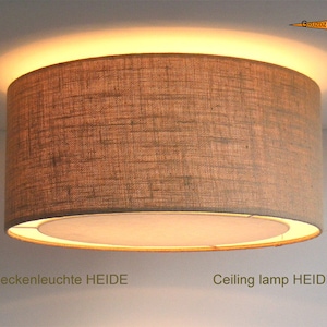 May include: A cylindrical ceiling lamp with a textured, brown fabric shade. The lamp emits a warm, diffused light. The text "Ceiling lamp HEIDE" is visible.