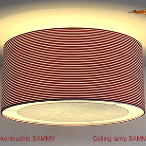 Könnte beinhalten: Eine rote Deckenleuchte mit einem gerippten Schirm und einem weißen Innenring. Die Leuchte ist mit "Deckenleuchte SAMMY" beschriftet.