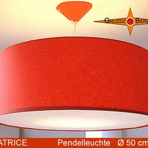Könnte beinhalten: Eine zylindrische Pendelleuchte mit einem leuchtend roten Stoffschirm und weißer Innenverkleidung. Die Leuchte umfasst einen passenden roten Deckenbaldachin und ein Kabel. Das Logo Gruzdz Berlin ist sichtbar, sowie der Text Beatrice Pendelleuchte 50 cm.