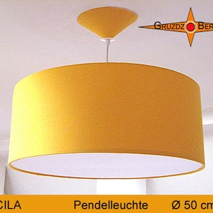 Könnte beinhalten: Eine gelbe zylindrische Pendelleuchte mit weißer Innenverkleidung, aufgehängt an einem weißen Kabel mit passendem gelben, konischen Deckenbaldachin. Der Text GRUZDZ BERLIN ist oben rechts und LUCILA Pendelleuchte Ø 50 cm unten zu sehen.