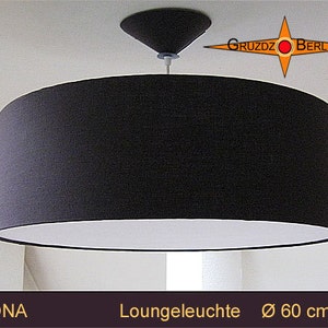 Pode incluir: Uma luminária pendente com um abajur de tambor de tecido preto e forro interior branco. A luminária está suspensa de um teto branco. A luminária é etiquetada como "Mona" e "Lounge Leuchte Ø 60 cm".