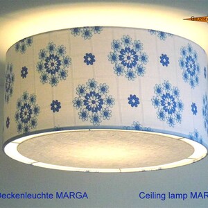 Może przedstawiać: Biała lampa sufitowa z niebieskim wzorem kwiatowym. Klosz jest cylindryczny i ma białe wnętrze. Lampa jest oznaczona jako "Lampa sufitowa MARGA".