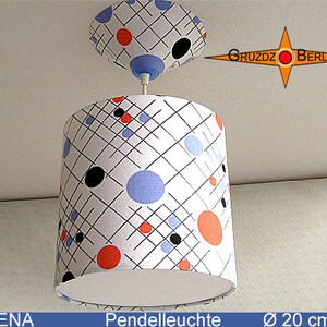 Puede incluir: Una lámpara colgante blanca con un patrón geométrico blanco y negro y círculos rojos, naranjas y azules. La luz tiene un diámetro de 20 cm. La luz está etiquetada como "VERENA" y "Pendelluchte".