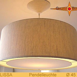 May include: A beige fabric drum pendant light fixture with a white inner shade. The light is hanging from a white ceiling fixture. The light is 45 inches in diameter. The text "MELISSA" and "Pendelluchte" is visible in the image.
