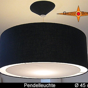 Può includere: Una lampada a sospensione cilindrica nera con un diffusore bianco sul fondo, appesa tramite un cavo a un rosone nero. Il testo GRUZDZ BERLIN appare in alto a destra, mentre UTA Pendelleuchte Ø 45 cm è riportato in basso.