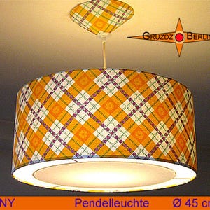 Könnte beinhalten: Zylindrische Pendelleuchte mit gelb-orange-weißem Karomuster. Die Lampe hat einen passenden Deckenbaldachin und einen Durchmesser von 45 cm. Das Wort "SUNNY" ist unten aufgedruckt.