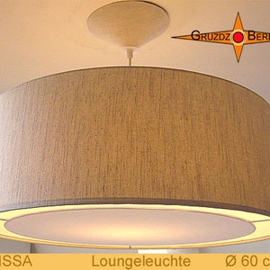 Könnte beinhalten: Eine Pendelleuchte mit einem beigefarbenen Stoffschirm in Trompetenform und einem weißen Innenschirm. Die Leuchte hängt an einer weißen Deckenhalterung. Die Leuchte ist mit "MELISSA Loungeleuchte Ø 60 cm" beschriftet.