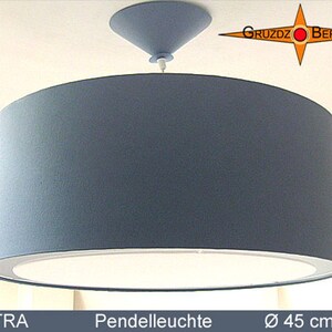 May include: A cylindrical pendant light with a solid grey fabric shade and a white bottom diffuser. The fixture features a matching grey conical ceiling canopy. The text GRUZDZ BERLIN is visible in the corner, with PETRA Pendelleuchte Ø 45 cm below.