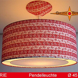 Può includere: Una lampada a sospensione cilindrica con paralume in tessuto a motivo floreale rosso e bianco. Il supporto a soffitto riprende lo stesso motivo. Il testo GRUZDZ BERLIN appare in alto a destra, e MARIE Pendelleuchte Ø 45 cm in basso.