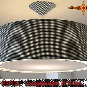 Könnte beinhalten: Eine große, runde Pendelleuchte mit einem schwarz-weißen Karomuster. Die Lampe hat eine passende Deckenhalterung und einen weißen Innenraum, der das Licht streut. Der Durchmesser beträgt ca. 70 cm.