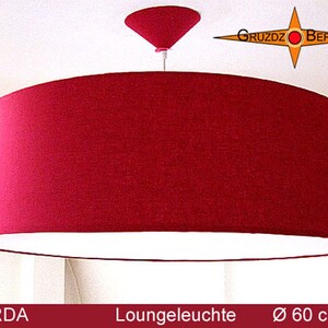 Könnte beinhalten: Eine große, zylindrische Pendelleuchte mit einem tiefroten Stoffschirm und einem weißen Diffusor an der Unterseite. Die Leuchte hängt an einem dünnen Kabel an einem passenden roten, konischen Deckenbaldachin. Text GRUZDZ BERLIN.
