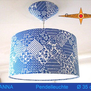 Könnte beinhalten: Eine zylindrische Pendelleuchte mit blau-weißem Patchwork-Muster aus Blumen-, Punkt- und Streifenmotiven. Die Leuchte verfügt über einen passenden Deckenbaldachin und einen Durchmesser von 35 cm. Das Logo Gruzdz Berlin ist zu sehen.