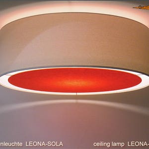 May include: A beige ceiling lamp with a red inner lining. The lamp is called "LEONA-SOLA" and is a ceiling lamp.