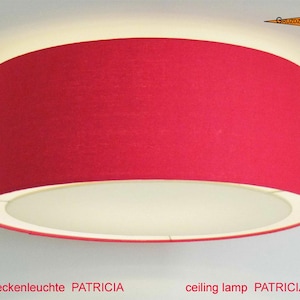 Könnte beinhalten: Eine runde Deckenleuchte mit einem leuchtend roten Stoffschirm in Trommelform und einer weißen Diffusorplatte an der Unterseite. Die Lampe strahlt ein sanftes Licht aus. Der Text "Deckenleuchte PATRICIA" ist unten und ein Logo oben zu sehen.