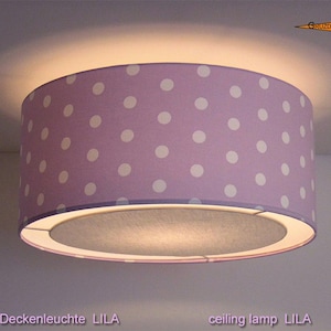 Könnte beinhalten: Eine zylindrische Deckenleuchte mit einem hellvioletten Stoffschirm, der mit einem sich wiederholenden Muster aus weißen Punkten versehen ist. Die Lampe leuchtet und wirft einen sanften Schein an die Decke, inklusive Text GRUZDZ BERLIN.