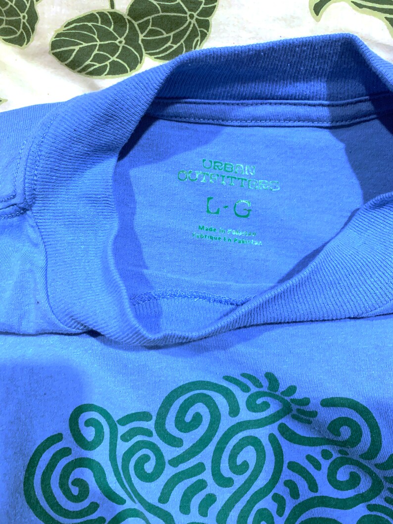 May include: A blue t-shirt with a green swirl design and the text "Urban Outfitters" and "L-G" printed on the front.