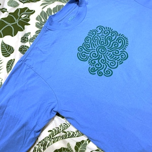 May include: A light blue long-sleeved t-shirt with a green abstract design on the front.