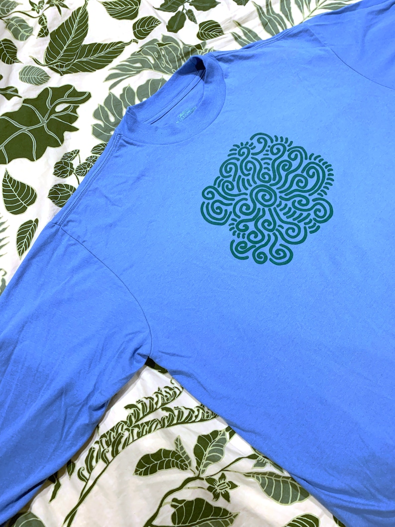 May include: A light blue long-sleeved t-shirt with a green abstract design on the front.