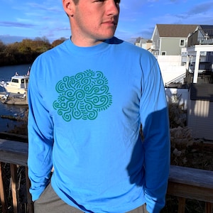 May include: A light blue long-sleeved t-shirt with a green abstract design on the front.