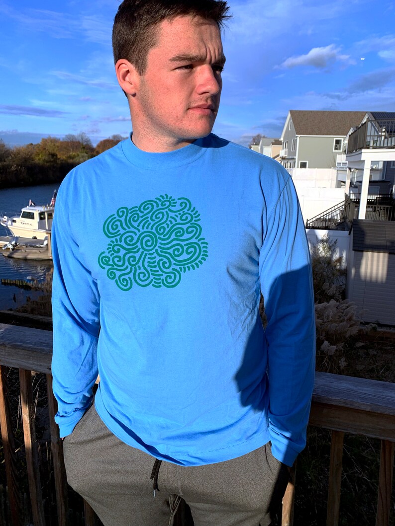 May include: A light blue long-sleeved t-shirt with a green abstract design on the front.