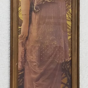 May include: A framed vintage print of a woman in a long, flowing, pink dress with lace details. The woman is standing in a garden setting with a yellow background.