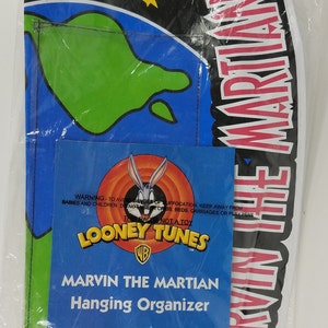 May include: A white plastic bag with a blue and green image of Marvin the Martian on the front. The bag contains a 37-inch long hanging organizer for toys, books, and more. The bag has a warning to keep away from babies and children. The bag is not a toy. The bag is made in China.