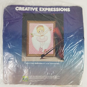 May include: A close-up of a craft kit featuring a ballerina with a pink tutu and a cello. The kit includes 100% cotton embroidery floss, tricot backing, polyester batting, a needle, and instructions. The kit is designed for a 11" x 14" project. The kit is from Creative Expressions.