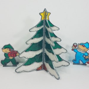 May include: A set of Christmas-themed figurines, including a green tree with white snow, a reindeer, a girl holding a heart, a boy holding a gift, a blue elf holding a candy cane, a green elf holding a wreath, and Santa Claus.