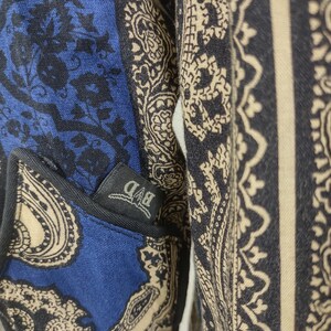 May include: A blue and beige paisley patterned shirt with a black pocket that has a white "BAD" label.
