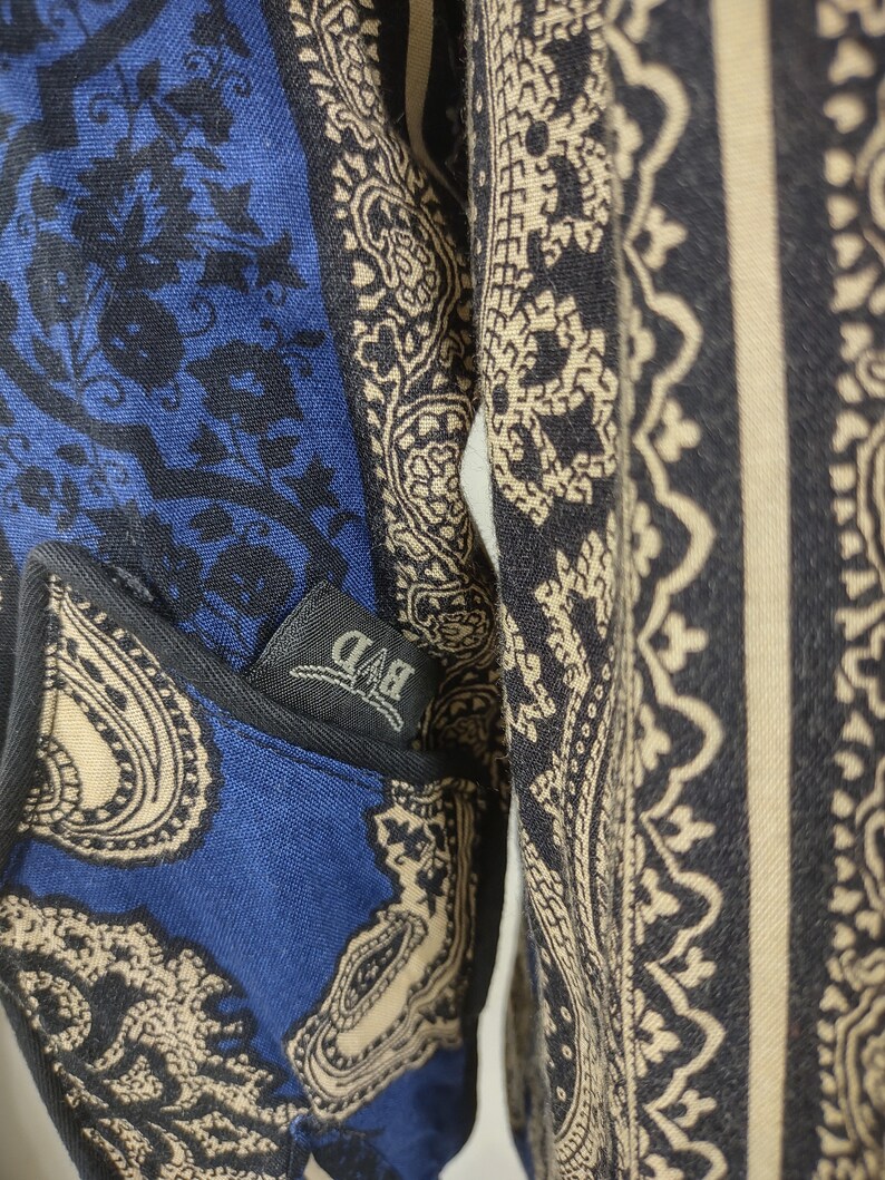 May include: A blue and beige paisley patterned shirt with a black pocket that has a white "BAD" label.