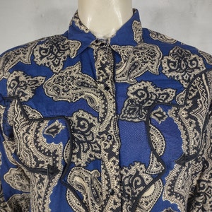 May include: A blue and cream paisley print long-sleeve shirt with a button-up front and black trim around the pockets.