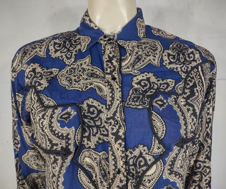May include: A blue and cream paisley print long-sleeve shirt with a button-up front and black trim around the pockets.