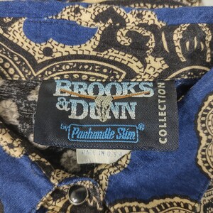 May include: A blue and tan paisley patterned shirt with a black label that reads "Brooks & Dunn by Panhandle Slim" and "Collection" in white text.