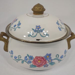 May include: White enamel pot with a floral design and brass handles and lid knob. The pot has a gold trim around the top.