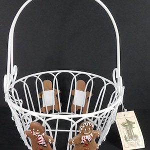 May include: White wire basket with a handle, decorated with gingerbread people. The basket has a tag attached that reads "Dennis East Creations, North Hampton, NH".