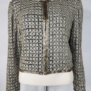 May include: A black sequined jacket with a gold floral pattern. The jacket has a front zipper closure and long sleeves.