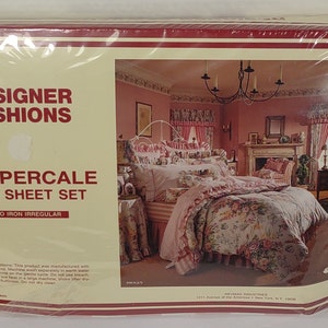 May include: A packaged Designer Fashions 200 Percale One Sheet Set. The packaging is cream-colored with a red border and features a picture of a bedroom with floral bedding. The text "DESIGNER FASHIONS" and "200 PERCALE ONE SHEET SET" are printed on the front.