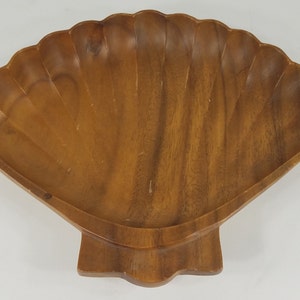 May include: A wooden serving dish shaped like a seashell. The dish is made of light brown wood and has a smooth, polished finish.