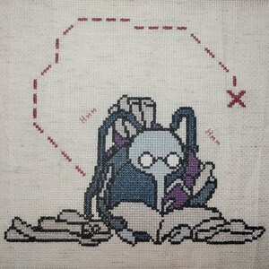 May include: Cross-stitch embroidery of a character with glasses reading a book, surrounded by scrolls. The character is wearing a blue and purple robe and has a thought bubble above their head that says "Hmm".
